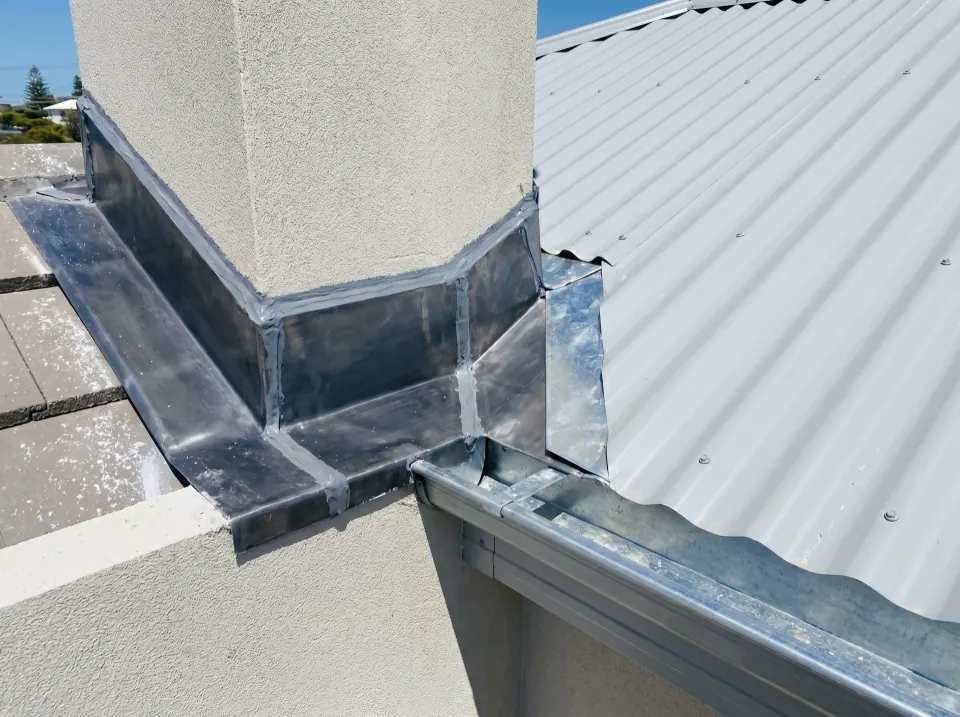 Close-up of new lead flashing and valley irons sealed where the roof meets a wall